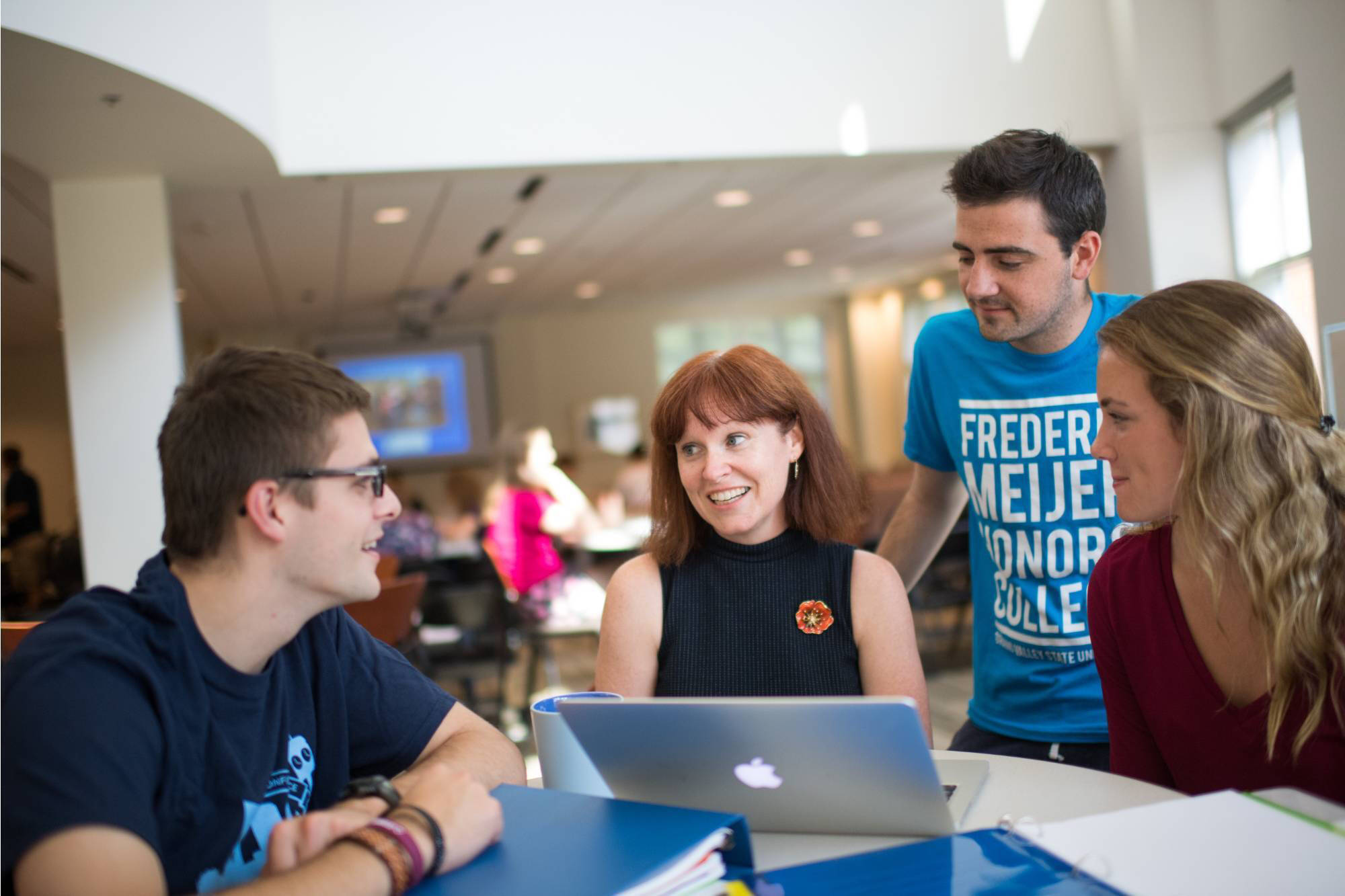 A group of Honors students engaging in a friendly discussion around a table with a laptop, books, and focus in a bright room.